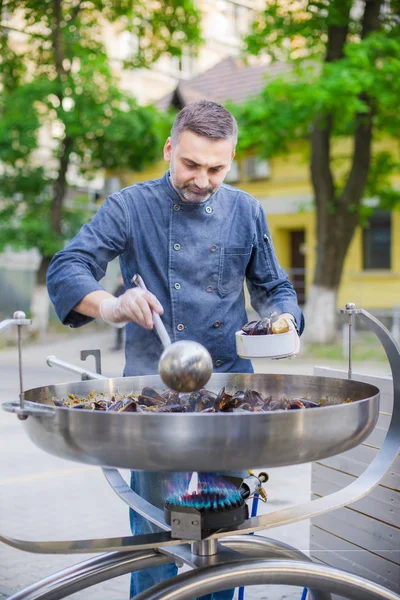 Кухар готує мідії у великій сковороді на вулиці — стокове фото