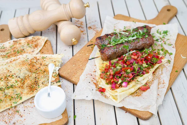 Kebab y Gozleme. Tradicional kebab oriental de carne de res picada o cordero con verduras y hierbas sobre el jabalí de corte de mármol. Gozleme con hierbas y queso . — Foto de Stock