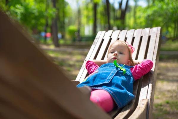 Веселый ребенок лежит на деревянной скамейке в солнечный день — стоковое фото