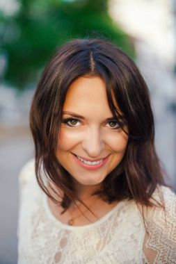 Gülümseyen, çerçeve içine bakan, arka sokakta beyaz bir elbise içinde güneşli bir şehir merkezinde ziyaret genç güzel kadın, siyah saçlı. Açık portre.