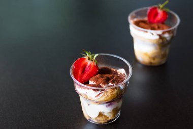 Lezzetli taze soğuk çilek peynir kek, tatlı koyu arka plan üzerinde plastik bardak. Kopya alanı