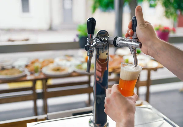Un hombre saca cerveza de un grifo en un vaso. Cerveza. El barman vierte cerveza en un vaso. Bar con cerveza en la terraza del restaurante . — Foto de Stock