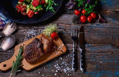 Sebze ve otlar bir kopya alanı ile kaba ahşap masa üzerinde bir rustik ahşap tahta üzerinde domuz biftek. Yatay.