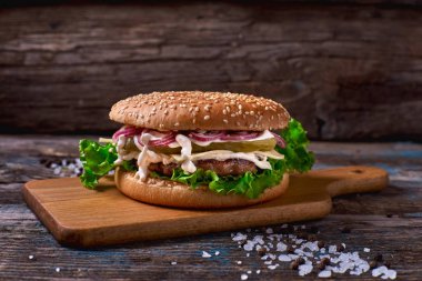 Çizburger et pirzola ve rustik ahşap yüzeyi koyu arka planı ve kopya alanı ile ahşap kesme tahtası üzerinde Turşu sebze ile