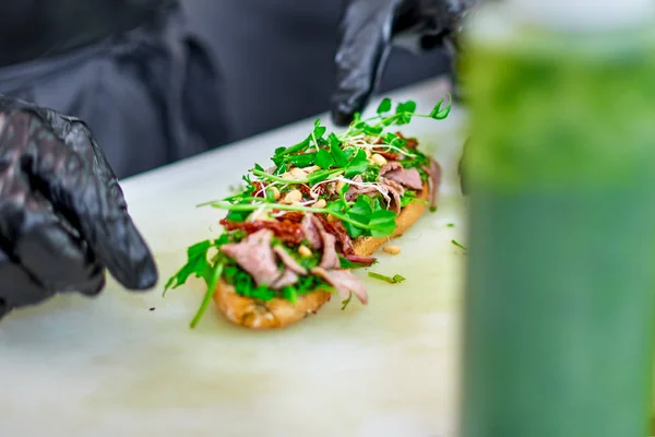 Накладний знімок рук шеф-кухаря, який готує смачні бришетти, додаючи до презентації листя ракет — стокове фото