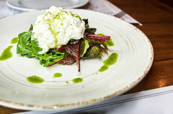 Especialidad italiana tradicional Queso Burrata en plato de cerámica servido con aceite de oliva y ensalada verde sobre una mesa de madera rústica blanca . —  Fotos de Stock