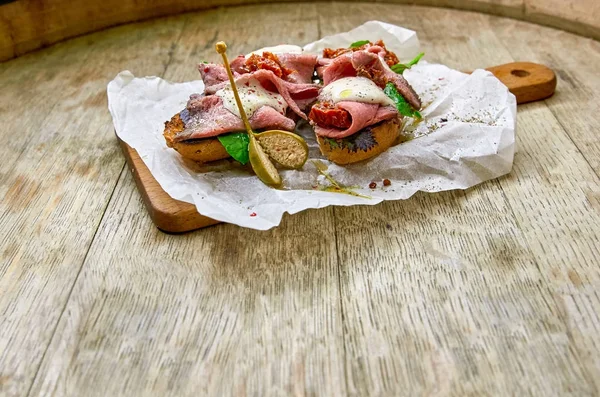 Dois bruschetta com presunto fresco e salada nas mãos de uma tábua de madeira close-up. Estilo de vida saudável . — Fotografia de Stock