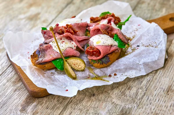 Dois bruschetta com presunto fresco e salada nas mãos de uma tábua de madeira close-up. Estilo de vida saudável . — Fotografia de Stock