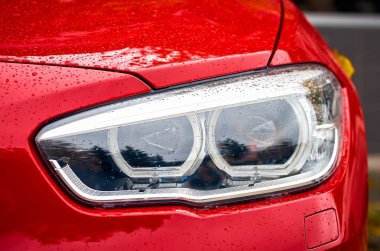 Yakın çekim Far üzerinde yağmur damlası ile kırmızı modern arabanın arka plan bulanıklık.