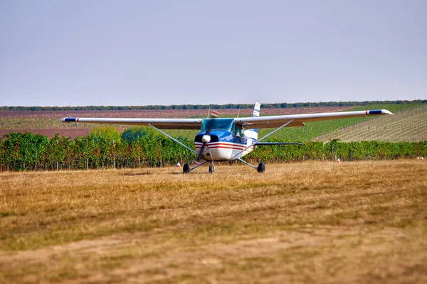 Uma aeronave leve pousa, em um campo perto de uma vinha. Dia de verão ensolarado, as pessoas assistem e plantam . — Fotografia de Stock