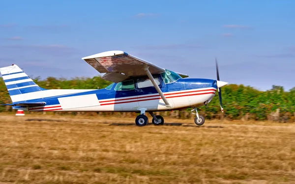 Uma aeronave leve descola em um campo perto de uma vinha. Dia de verão ensolarado, as pessoas assistem e plantam . — Fotografia de Stock