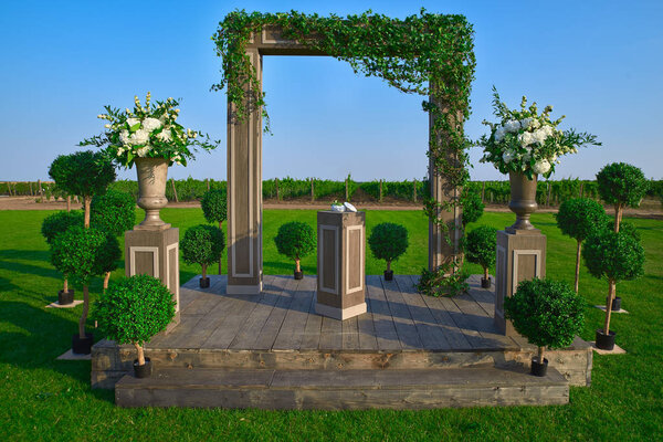 Свадебная арка украшена тканью и цветами на открытом воздухе. Прекрасная свадебная церемония. Свадебная церемония на зеленой лужайке в саду. Часть праздничного декора, цветочная композиция.