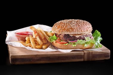 Burger siyah arka plan üzerine izole ahşap kesme tahtası üzerinde patates kızartması ile