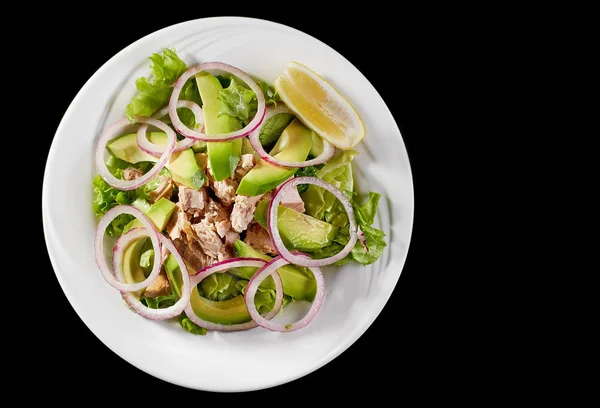 Salade de thon à l'avocat et roquette sur une assiette blanche, sur fond noir . — Photo