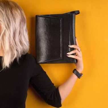 Modern siyah deri bir çantada bir kadın eli. turuncu arkaplan üzerinde poz vermek, metin ve tasarım için 1: 1 kopyalama alanı.