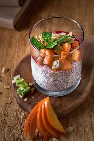 Jogurt deserowy z nasionami chia i owocami persymony na drewnianym ciemnym tle. Zdrowe wegańskie, wegetariański stół śniadaniowy, składniki na stole — Zdjęcie stockowe