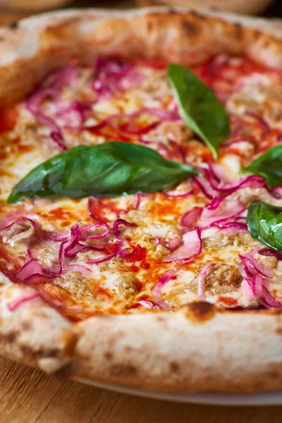 Italiaanse pizza met tonijn en rode ui op een houten plank in een rustieke keuken of pizzeria op een oude houten tafel — Stockfoto
