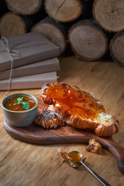 Vers gebakken croissant met abrikozenjam en tafel een lepel close-up op rustieke houten achtergrond — Stockfoto