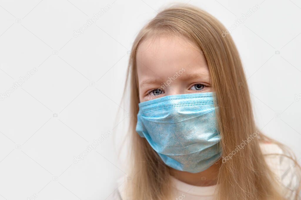 Portrait of a little blonde 6 years old with a medical mask on his face on a gray background, close up. Copy space.