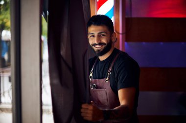Kuaföründe genç bir kuaför. Sakallı bir adam pencerenin yanında duruyor ve sokağa bakıyor..