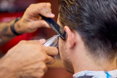 Usta berber dükkanında saç ve sakal kesiyor, kuaför genç bir adam için saç stili yapıyor. Berber dükkanında çalışmak, kuaförün işlemleri....