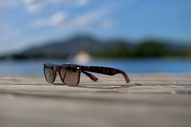 Güneş gözlükleri sahildeki masanın üzerinde deniz ve kıyı rıhtımında gün batımına doğru. Tatil, tatil ve rahatlama kavramsal fotoğrafçılık. Deniz kenarında ya da kıyıda eski ya da modern güneş gözlükleri.
