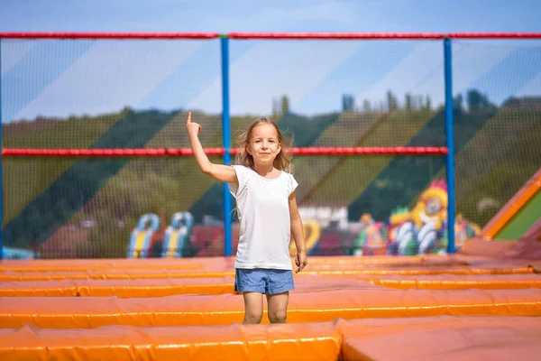 Little pretty girl having fun outdoor. Jumping on trampoline in children zone. Happy girl jumping on the yellow trampoline in Amusement park — Stock Photo, Image