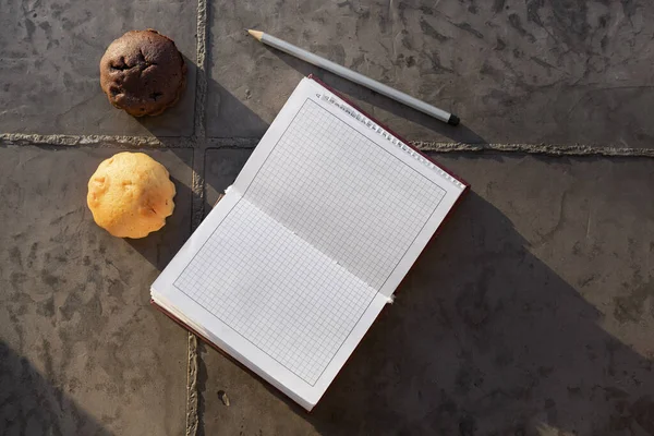 Open notebook and cupcake. Workspace with open notebook, on old Gray concrete background. Top view with space for your records.