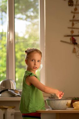 Küçük tatlı kız mutfakta yemek pişiriyor. Kurabiyelerin tadını çıkar. Kameraya bakarken fotoğrafının çekildiğini görünce şaşırdı..