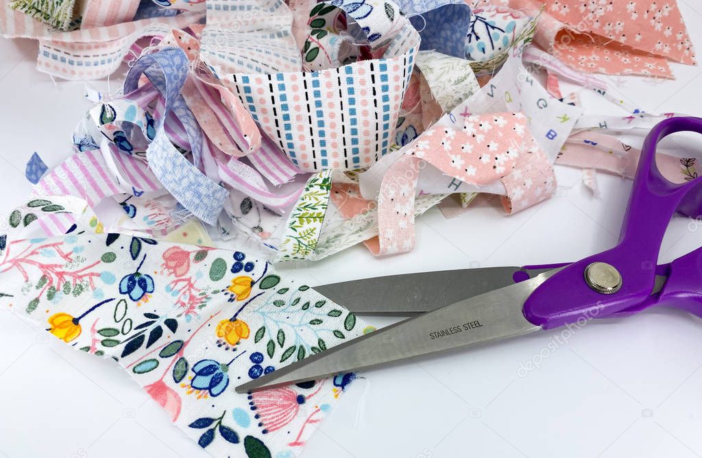 Close up view of a dressmaking scissors with a pile of scraps of printed patterned fabric
