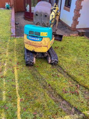 Cardiff, Wales - Şubat 2020: Çimenlik boyunca uzanan bir evin arka bahçesinde mini kazıcı