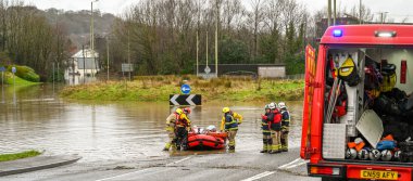NANTGARW, NEAR CARDIFF, WALES - FEBRUARY 2020: Firemen carrrying an elderly lady on an inflatable boat after evacuation due to flooding in Nantgarw. On the right is a specialist water rescue vehicle