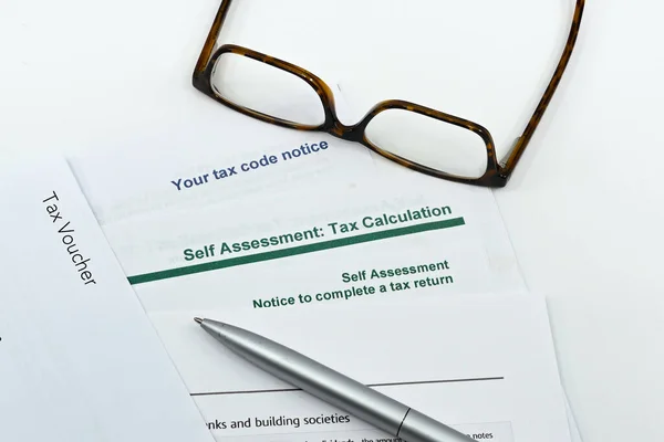 Close up view of a self assessment tax return form with a pen, a pair of glasses on a plain white background