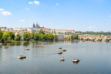 PRAGUE, CZECH REPUBLIC - JULY 2018: People on pedalo boats on the River Vltava, which runs through the centre of Prague. In the background is Prague Castle and St Vitas Cathedral.