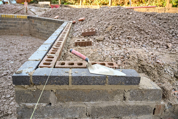 Bricklayer's trowel on top of a concrete block retaining wall around a garden.