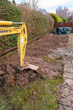 CARDIFF, WALES - JANUARY 2020: ucket and arm of a mini excavator digging up the lawn in the back garden of a residential property