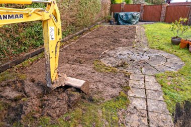 CARDIFF, WALES - JANUARY 2020: Bucket and arm of a mini excavator digging up the lawn in the back garden of a residential property
