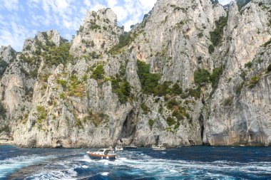 ISLE OF CAPRI, ITALY - AUGUST 2019: Small boats at sea on the rugged coastline of the Isle of Capri.