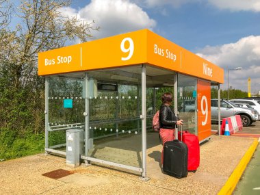 LONDON GATWICK AIPORT - APRIL 2019: Person with luggage waiting at a bus stop in the long term car park of London Gatwick Airport