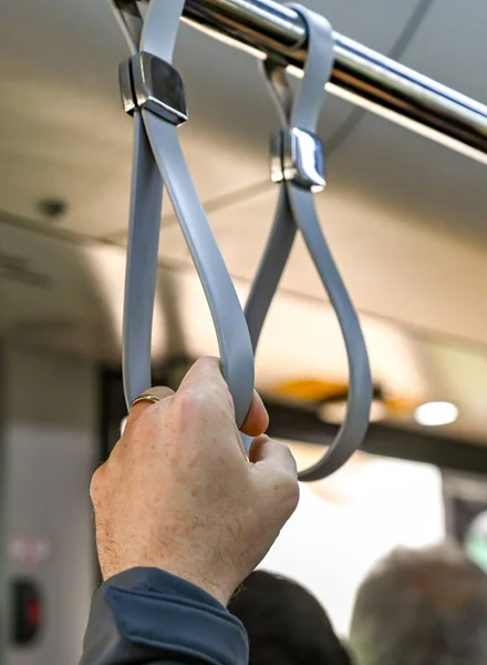 Person\'s hand holding on to a safety strap while travelling standing up in a bus