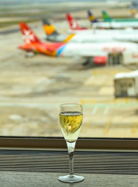 LONDON GATWICK HAVAALİ 2019: Londra Gatwick Havaalanı 'ndaki bir iş yerindeki pencere pervazında bir bardak şampanya. Arka planda jetlerin kuyruk yüzgeçleri var..