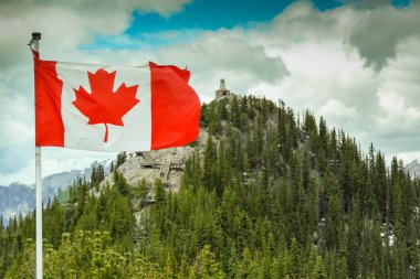 BANFF, AB, CANADA - Haziran 2018: Kanada Ulusal Bayrağı, Maple Leaf, Banff 'taki Sülfür Dağı' nda dalgalanıyor. Mesafelerde zirvede eski meteorolojik gözlemevi binası bulunuyor..