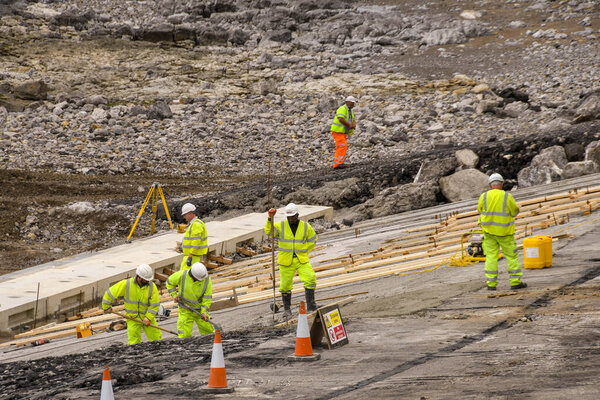 ПОРТКАУЛ, ОТКРЫТО - ИЮНЬ 2018: Строительные оперативники, работающие во время отлива над реконструкцией набережной в центре городской набережной
