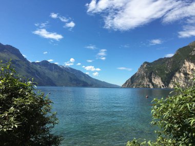 Riva del Garda, İtalya - Mayıs 2017: Arka planda yüksek dağlarla gölün berrak sularına bakan sahil manzarası