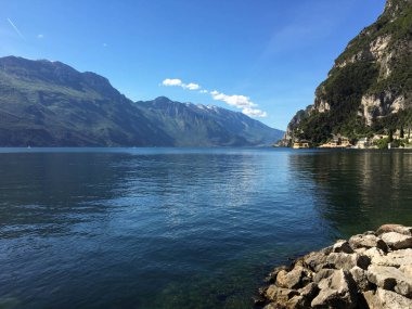 Riva del Garda, İtalya - Mayıs 2017: Arka planda yüksek dağlarla gölün berrak sularına bakan sahil manzarası