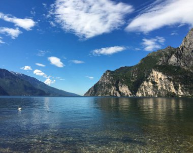 Riva del Garda, İtalya - Mayıs 2017: Arka planda yüksek dağlarla gölün berrak sularına bakan sahil manzarası