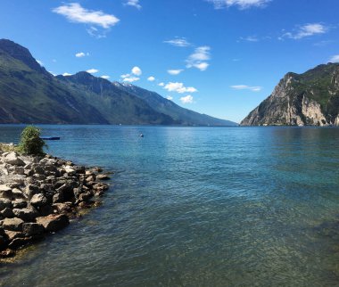 Riva del Garda, İtalya - Mayıs 2017: Arka planda yüksek dağlarla gölün berrak sularına bakan sahil manzarası