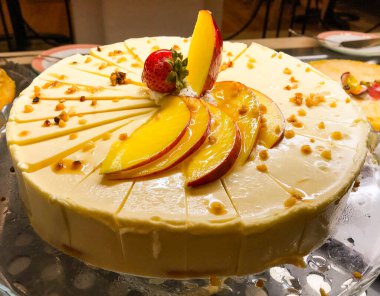 Şeftali dilimleri ve çilekle süslenmiş peynirli kek.