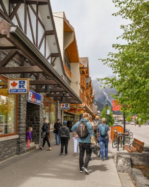BANFF, AB, CANADA - Haziran 2018: Banff 'ın merkezindeki dükkanların önünden geçen turistler.