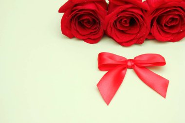 Üzerlerinde su damlaları olan üç kırmızı gül ve yanında kırmızı bir yay. Mutlu yıllar kartı.